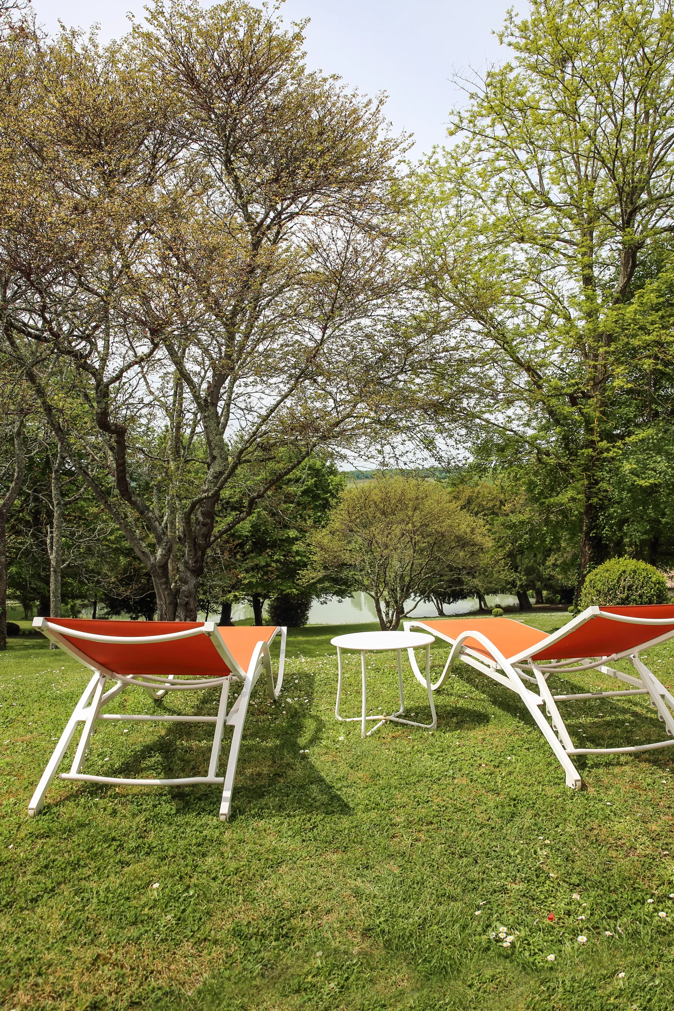 Deux transats orange sur pelouse face au lac.