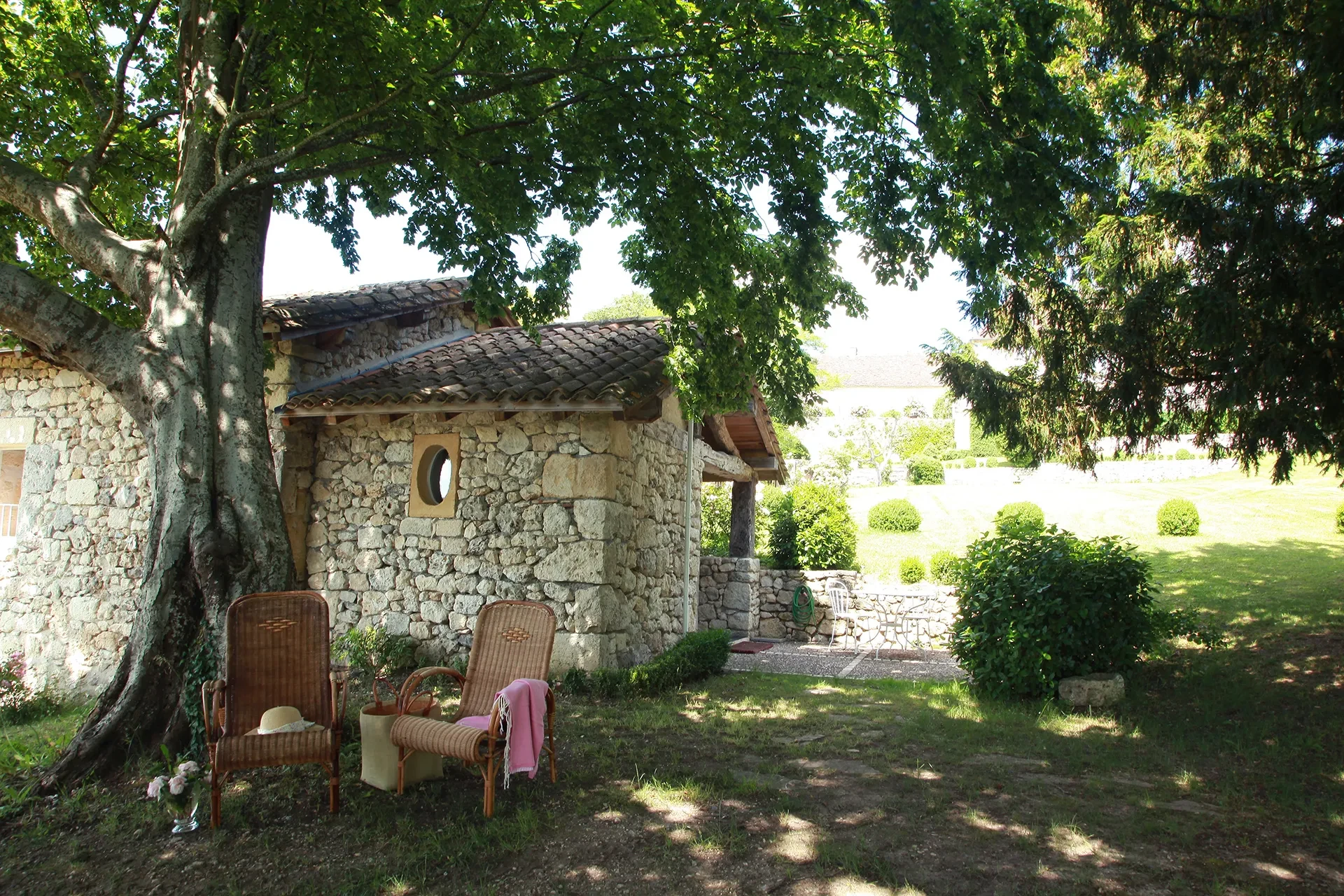 Maison en pierre avec chaises sous un arbre.