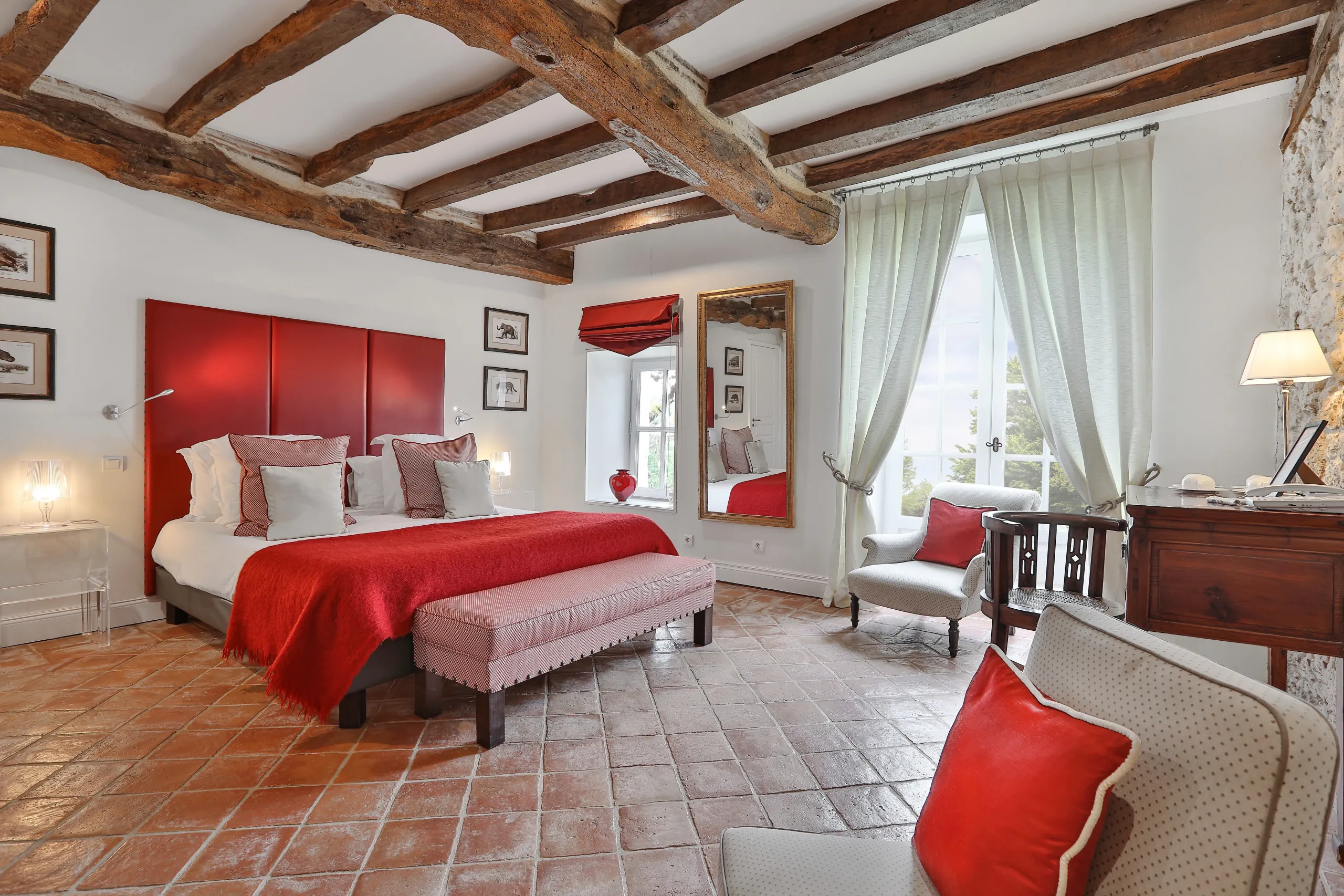 Chambre avec lit rouge et poutres apparentes.