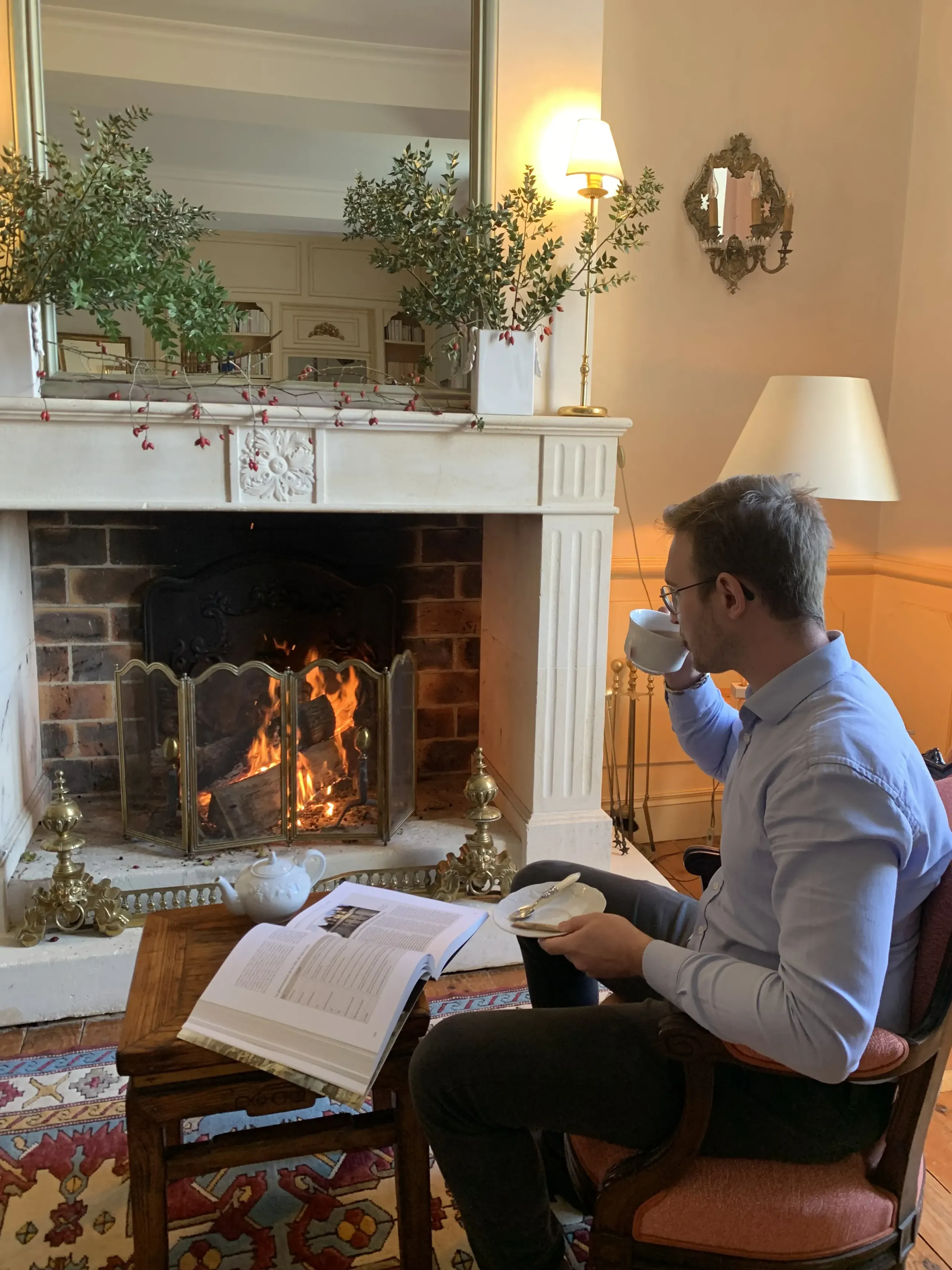 Homme lisant près d'une cheminée avec une tasse.