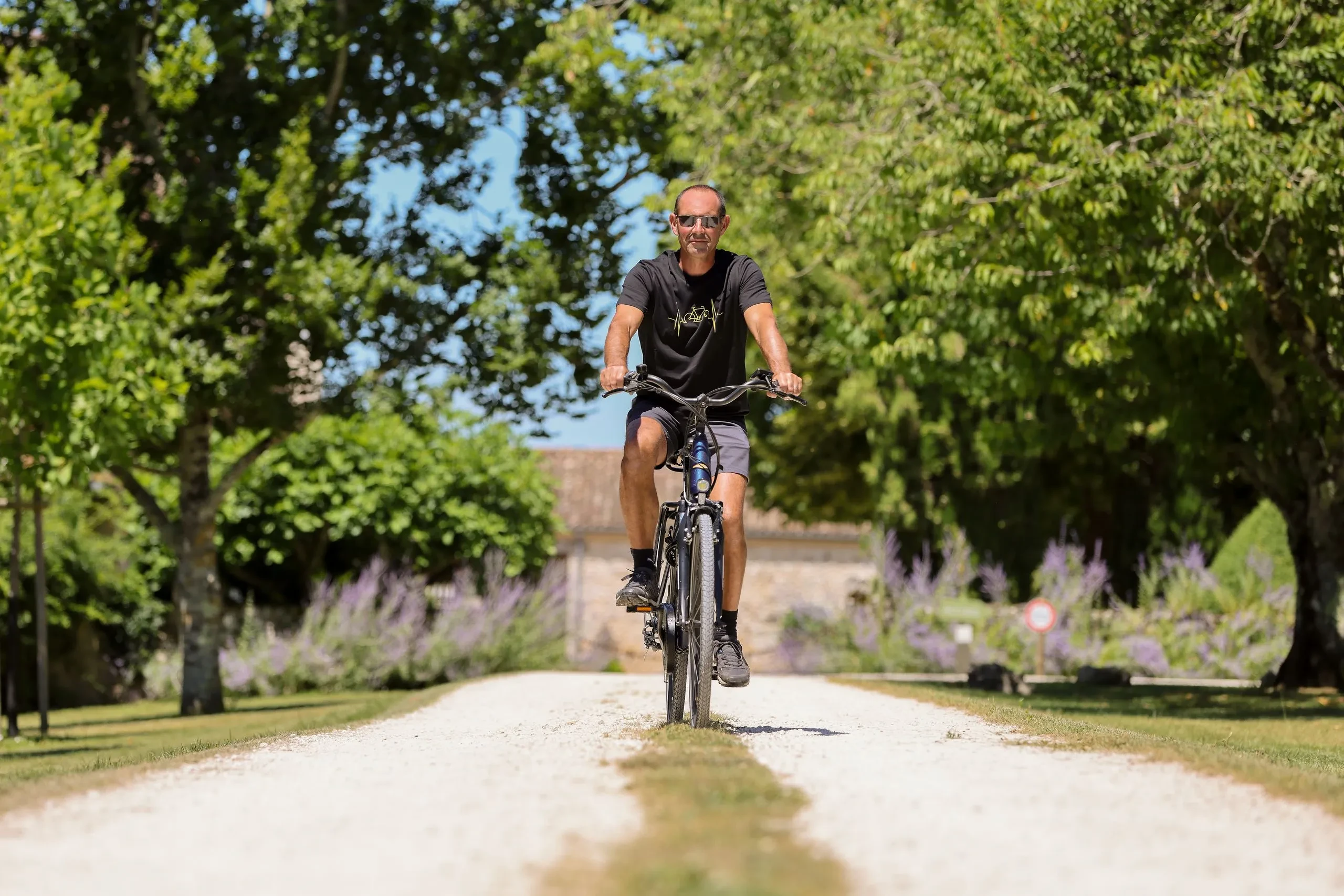 Homme faisant du vélo sur chemin bordé d'arbres.