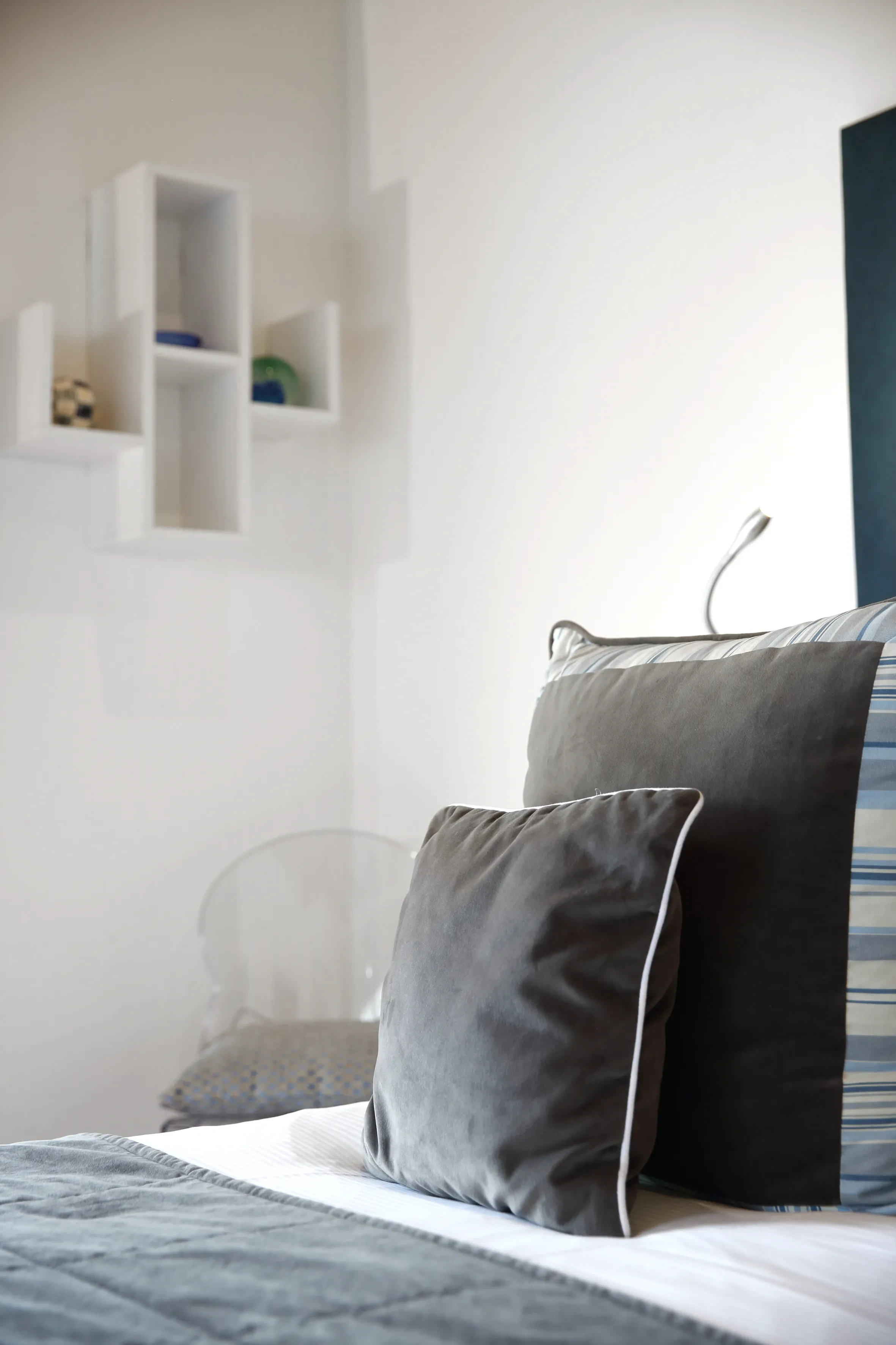 Chambre avec coussins gris et étagère murale blanche.
