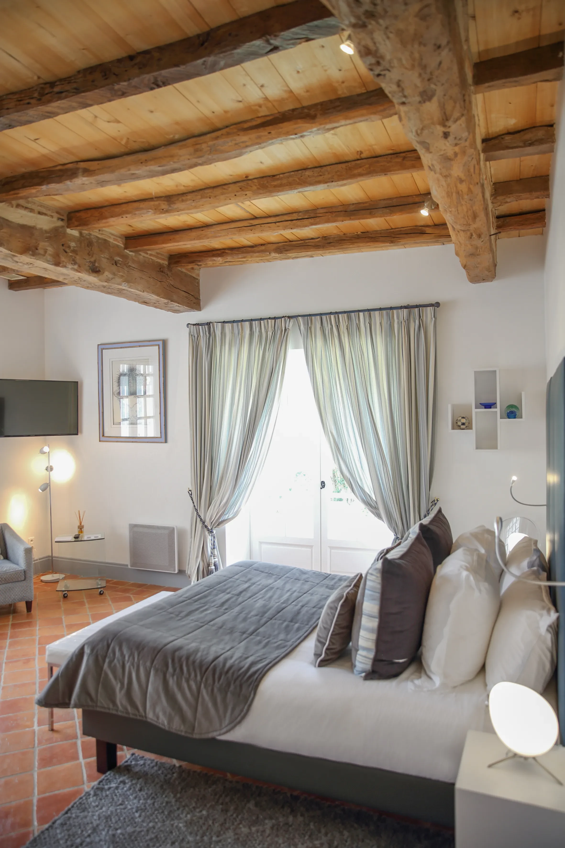 Chambre cosy avec lit, rideaux et poutres apparentes.