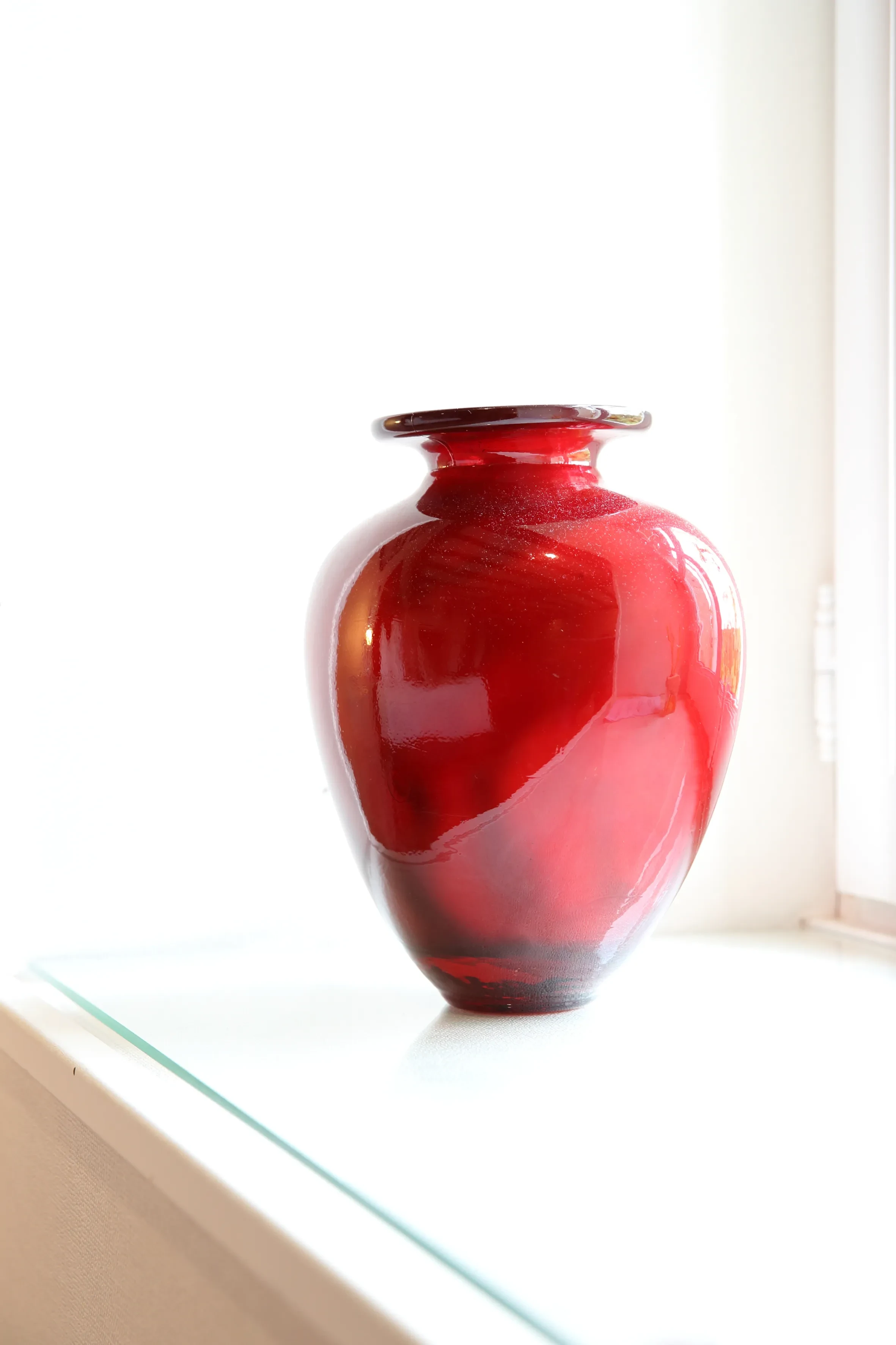 Vase rouge en verre sur étagère lumineuse.