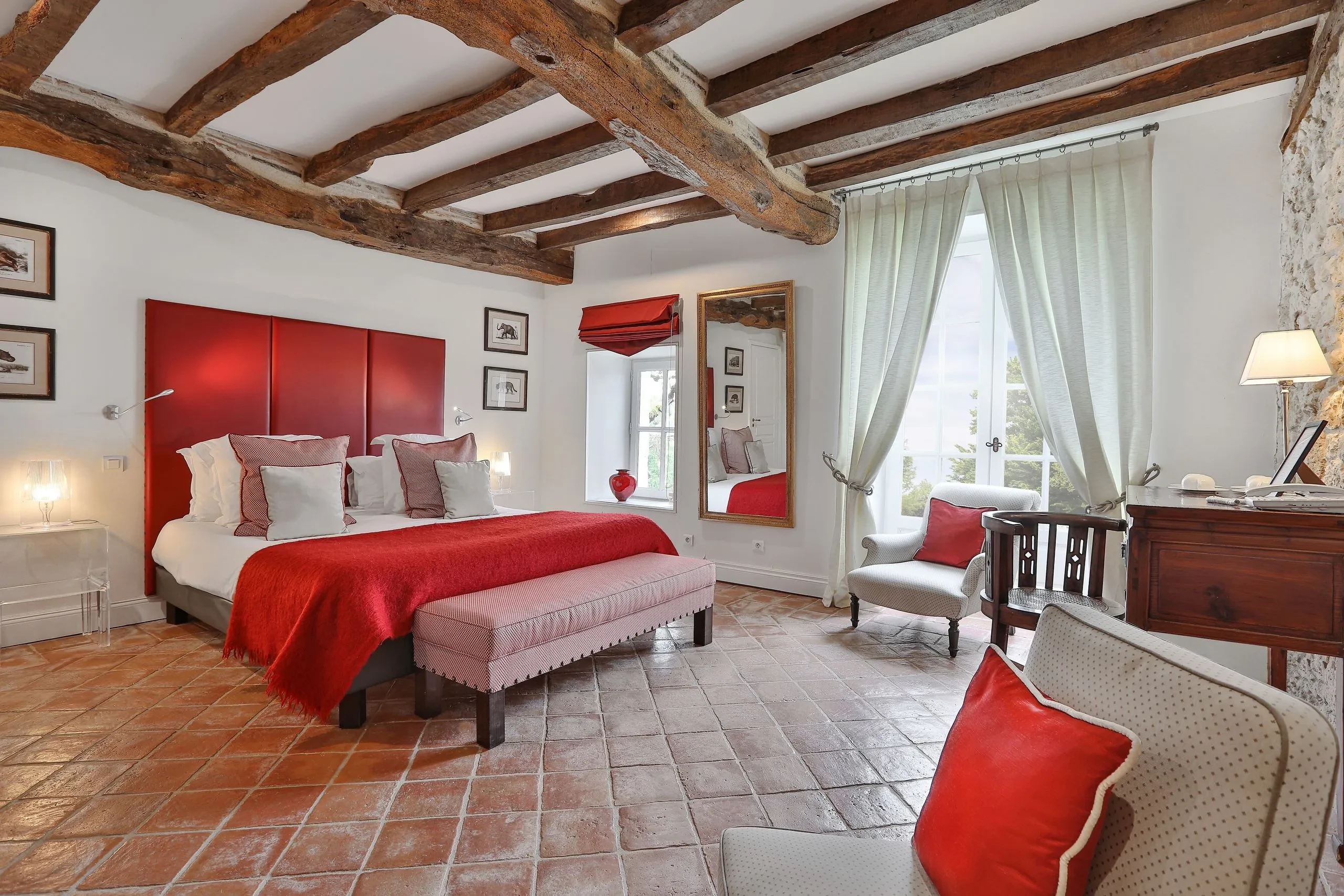 Chambre lumineuse avec literie rouge et poutres apparentes.