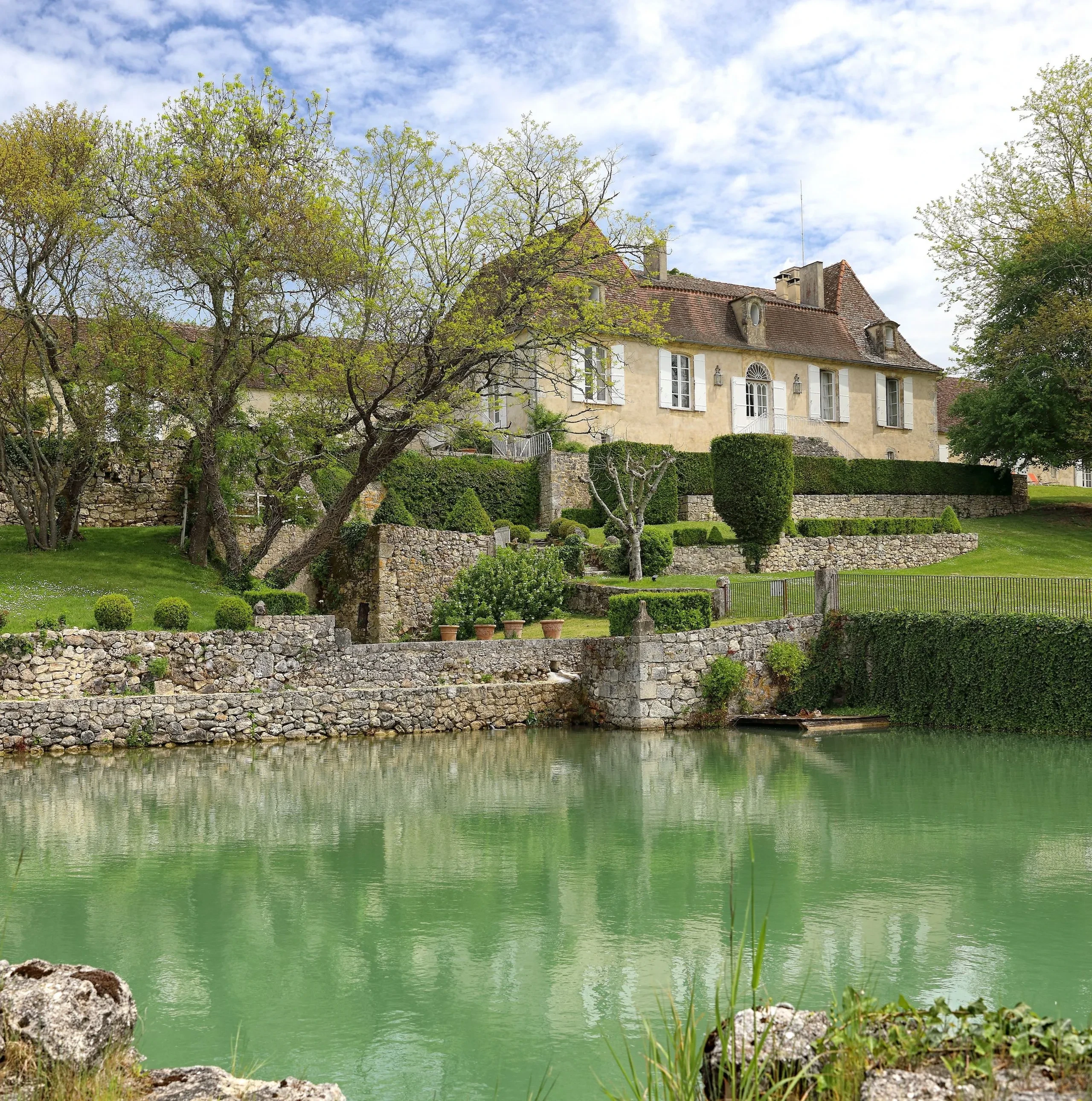 Maison en pierre près d'un étang verdoyant.