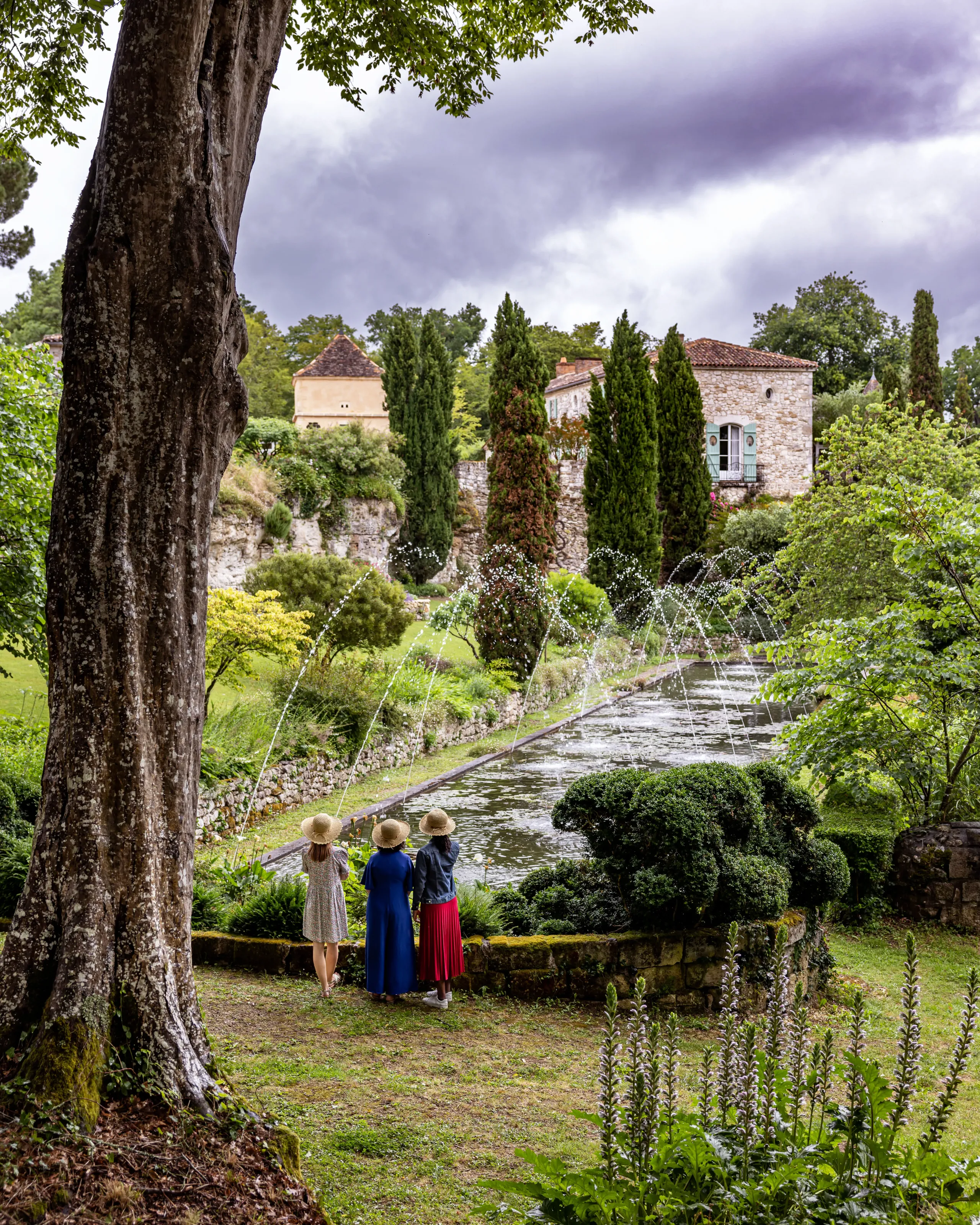 Trois femmes admirent un jardin et un manoir.